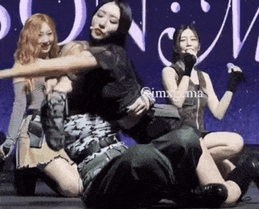 a group of women are dancing on a stage while a man is kneeling on the floor .
