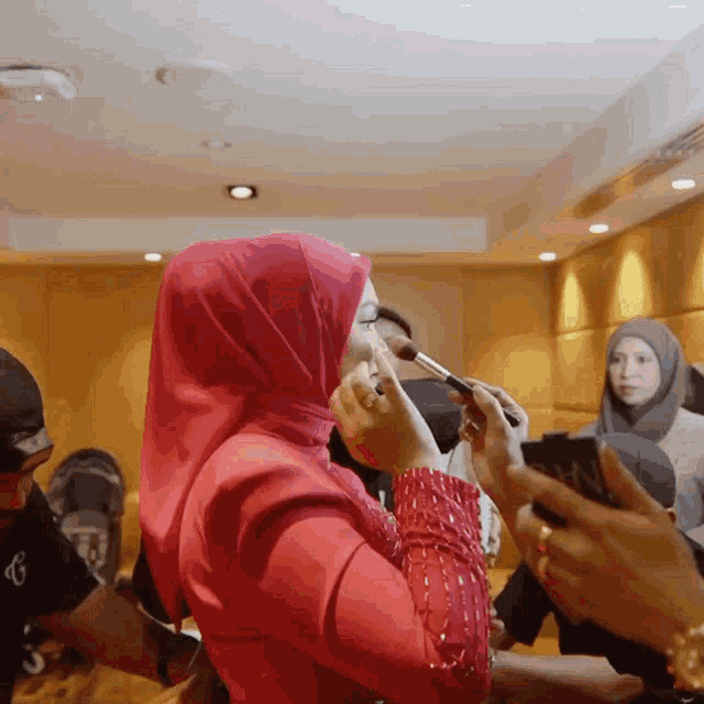 a woman wearing a pink hijab is applying makeup