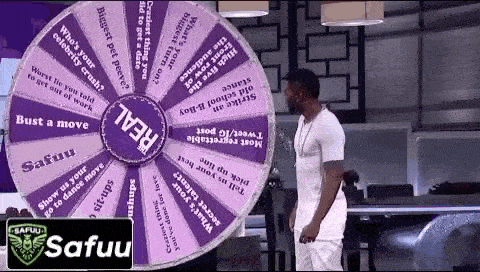 a man in a white shirt is standing in front of a wheel of fortune .