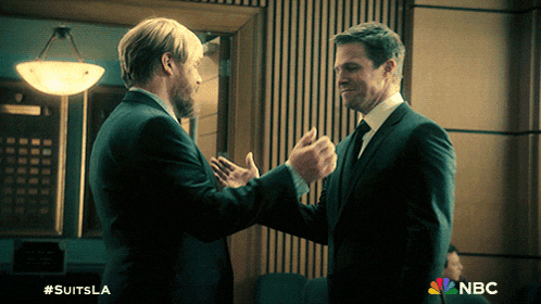 two men in suits shake hands in front of a sign that says nbc on it
