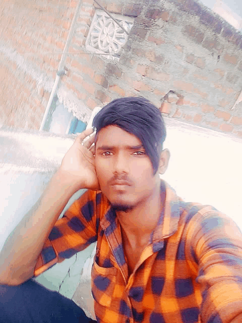 a young man in an orange and black plaid shirt is taking a selfie