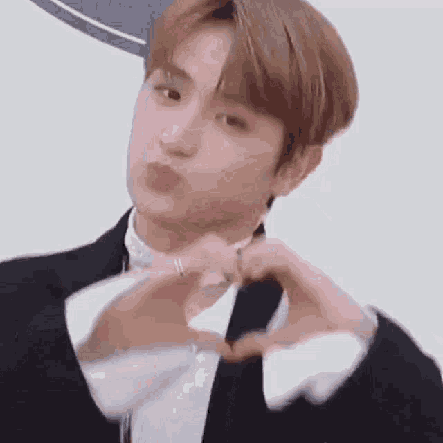 a young man in a suit is making a heart with his hands .