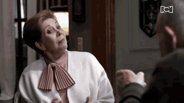 a woman in a white sweater and pink bow tie talks to a man in a suit