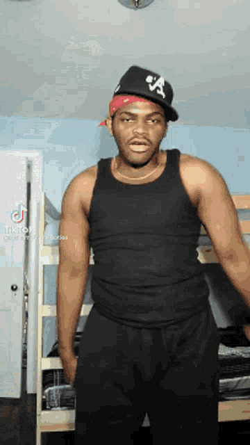 a man wearing a black tank top and a hat with the letter a on it