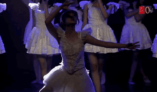 a group of women in white dresses are dancing on a stage with the letters jt on the bottom left