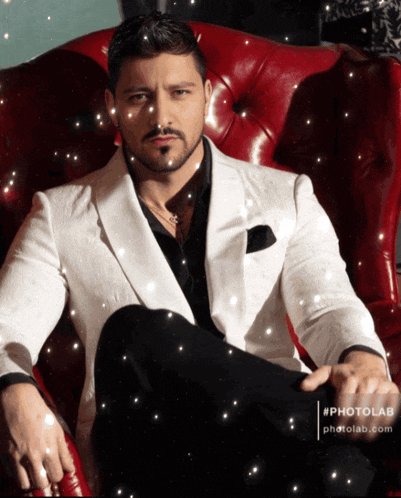 a man in a white suit sits on a red leather chair
