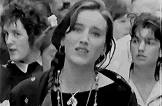 a woman is standing in a crowd of people and looking at the camera .