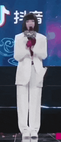 a woman in a white suit is standing on a stage with a microphone .