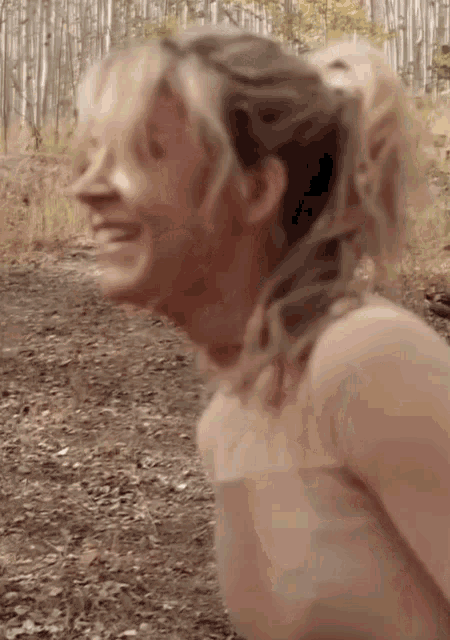 a naked woman is standing in the woods smiling .