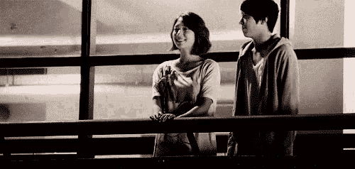 a man and a woman are standing next to each other on a balcony looking out of a window .