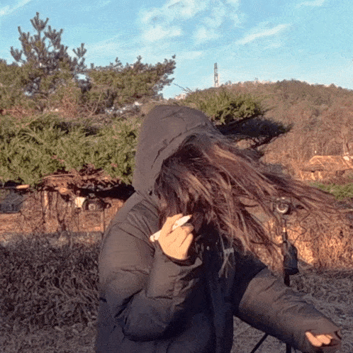 a woman wearing a black jacket with a hood is blowing her hair in the wind