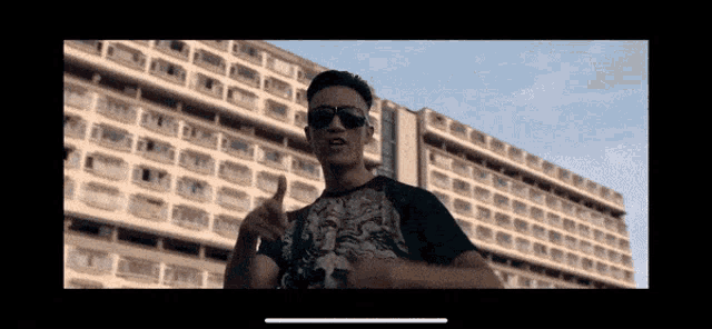 a man wearing sunglasses stands in front of a large building