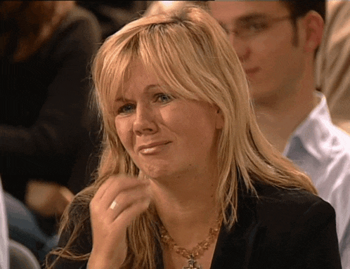 a woman with blonde hair and a gold necklace is sitting in a crowd of people