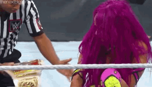 a woman with purple hair is wrestling another woman in a ring while a referee watches .