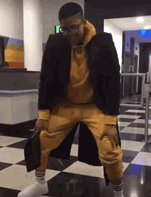 a man in a yellow hoodie and yellow sweatpants is kneeling on a checkered floor .