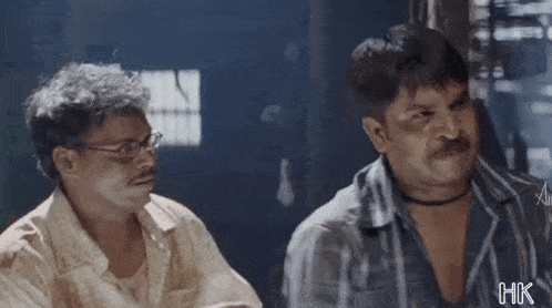 two men are sitting next to each other and looking at each other .