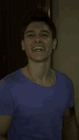 a man in a purple shirt is smiling and wearing a necklace .