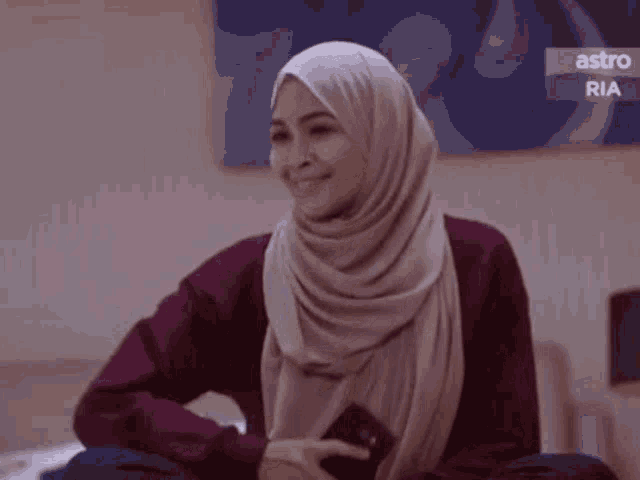 a woman in a hijab is smiling while looking at her cell phone .