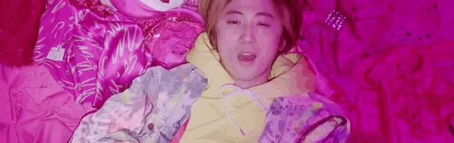a woman in a yellow hoodie is laying on a pink blanket on a bed .