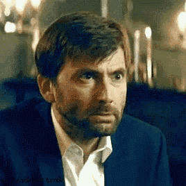 a man with a beard is wearing a suit and white shirt and looking at the camera .