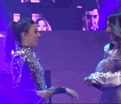 two women are hugging each other on a stage and they are wearing silver outfits