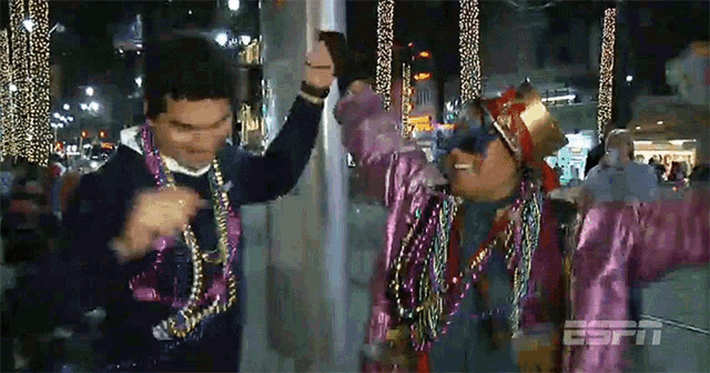 two men wearing mardi gras costumes are dancing in front of a espn sign
