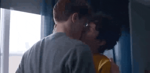 a couple of men kissing in front of a window .