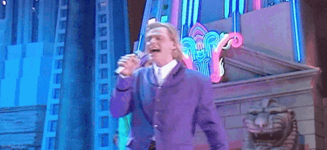 a man in a purple suit is singing into a microphone on a stage
