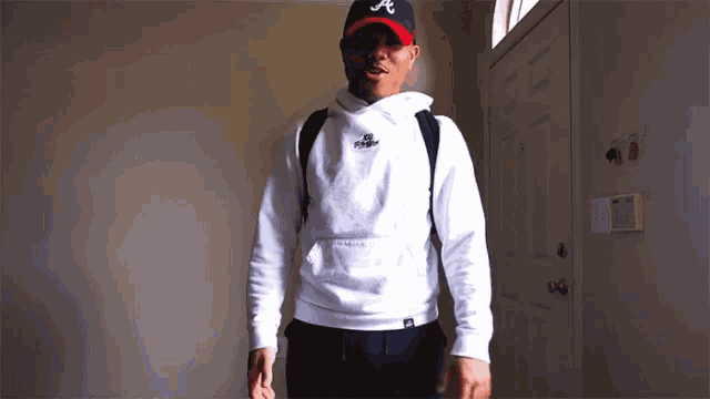 a man wearing a white hoodie and a baseball cap with the letter a on it