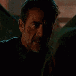 a man with a beard and blood on his face is looking at a woman in a dark room .