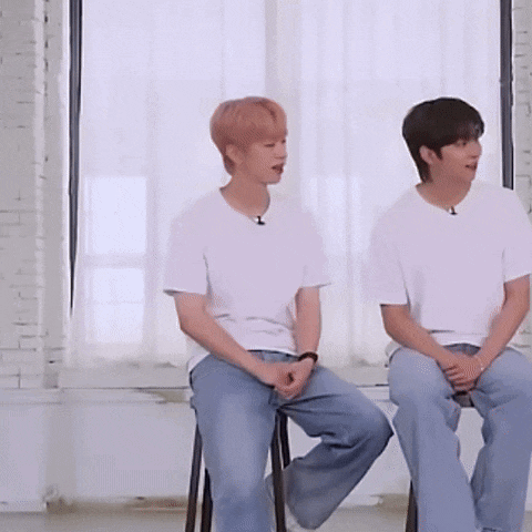 two men sitting on stools in front of a window