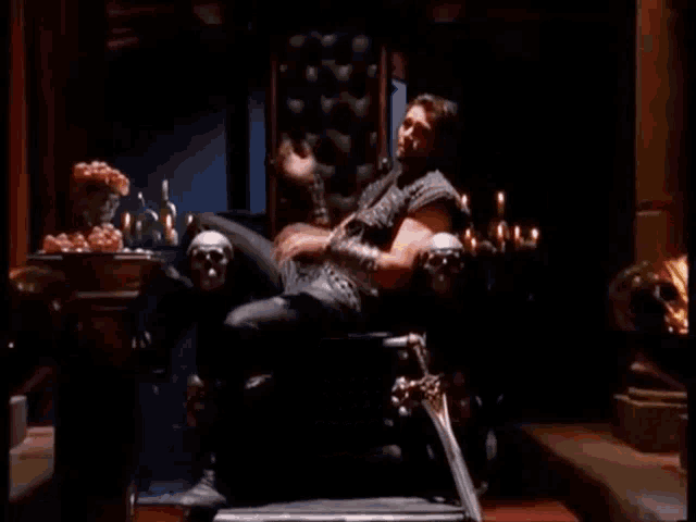 a man is sitting on a throne in a dark room with candles .