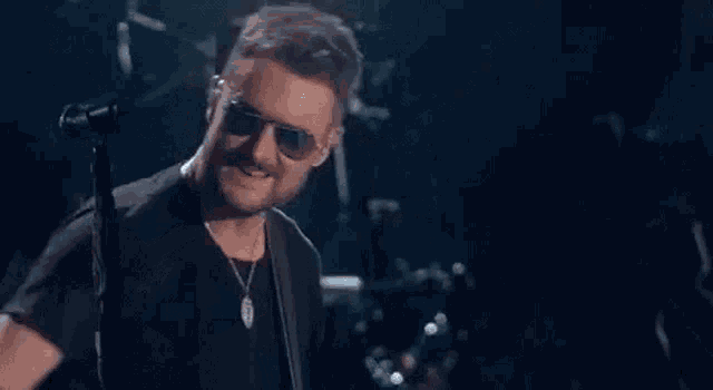 a man wearing sunglasses is singing into a microphone while playing a guitar on a stage .