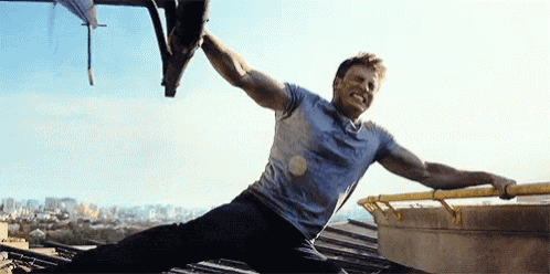 a man is sitting on a roof with his arms outstretched and a helicopter in the background .