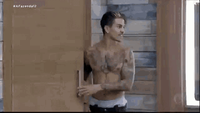 a shirtless man is standing in front of a wooden door in a room .