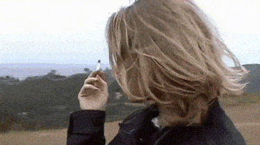 a woman smoking a cigarette in a field with mountains in the background