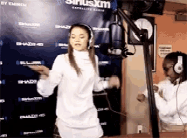 a woman in a white dress is dancing in front of a siriusxm sign