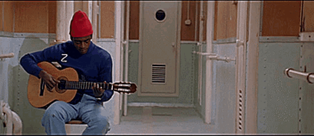 a man in a blue sweater with the letter z on it is playing a guitar