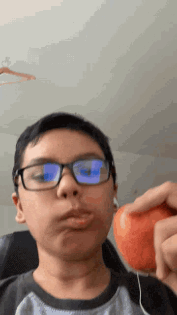 a young boy wearing glasses and ear buds is eating an apple