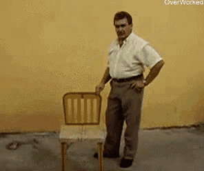 a man is standing next to a chair giving a thumbs up .