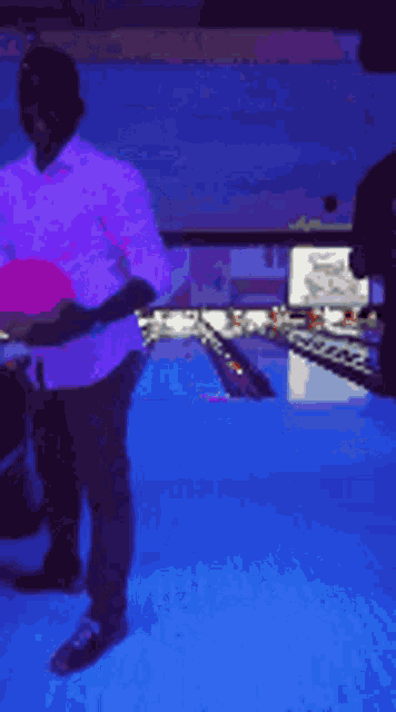 a man in a pink shirt is bowling in a dark bowling alley