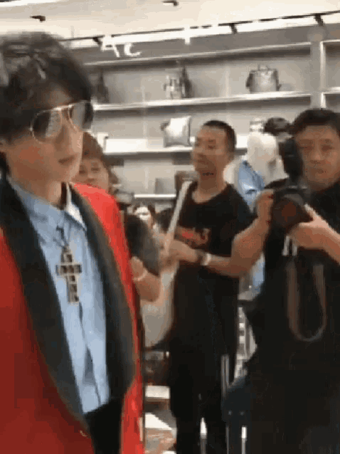 a man wearing sunglasses and a cross necklace is standing in front of a crowd of people .