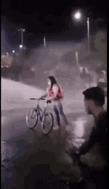 a woman is riding a bike down a street at night while a man watches .