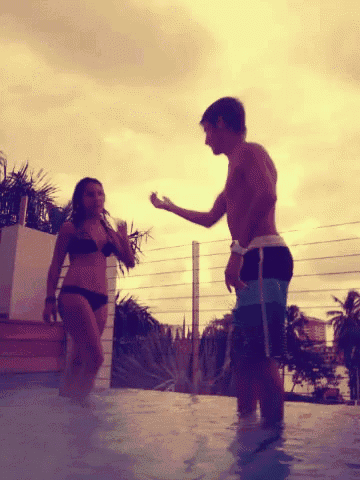 a woman in a bikini reaches out to a man in a swimming pool
