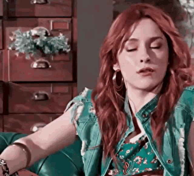 a woman with red hair is sitting on a couch with her eyes closed and wearing a green vest .
