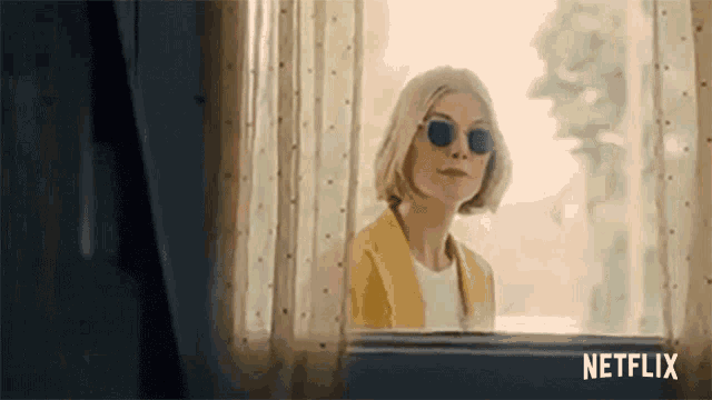 a woman wearing sunglasses is standing in front of a window .