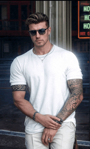 a man wearing sunglasses and a white shirt stands in front of a sign that says ho