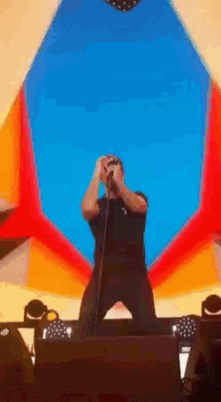 a man singing into a microphone on stage with a colorful background