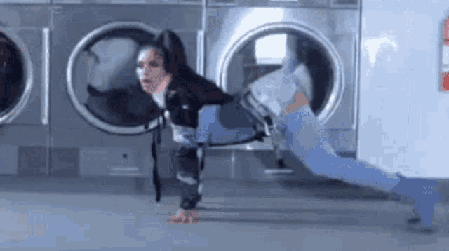 a woman is doing push ups in front of a washing machine in a laundromat
