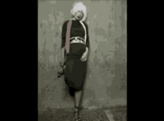 a woman in a black dress is standing in front of a grey wall